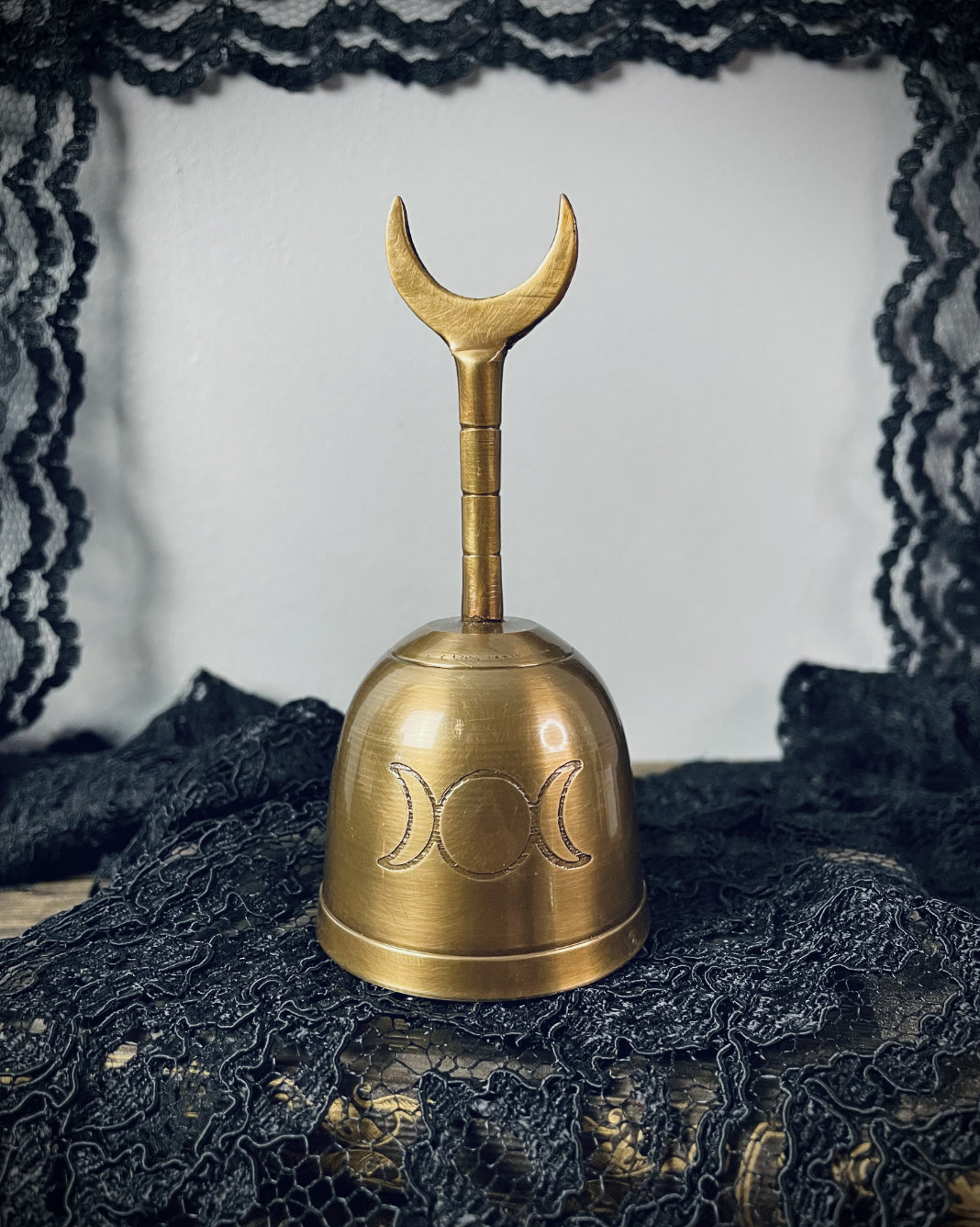 A brass hand bell marked with a triple moon glyph. Its handle ends in a crescent moon.