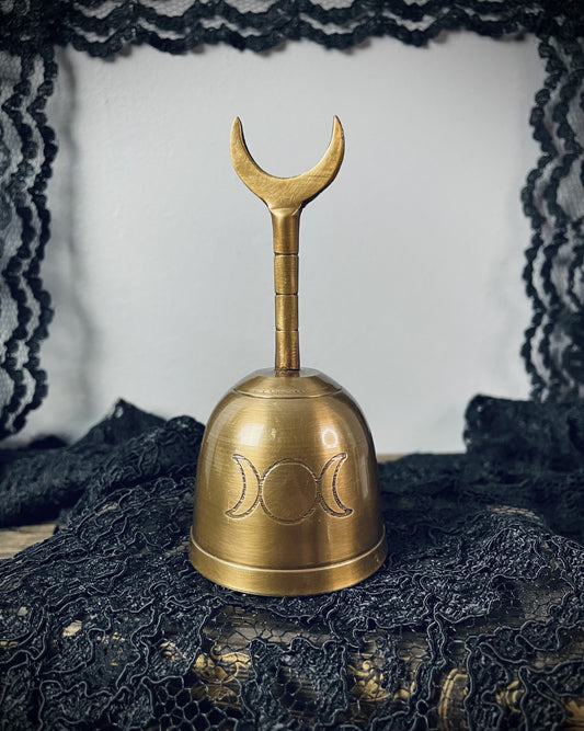 A brass hand bell marked with a triple moon glyph. Its handle ends in a crescent moon.