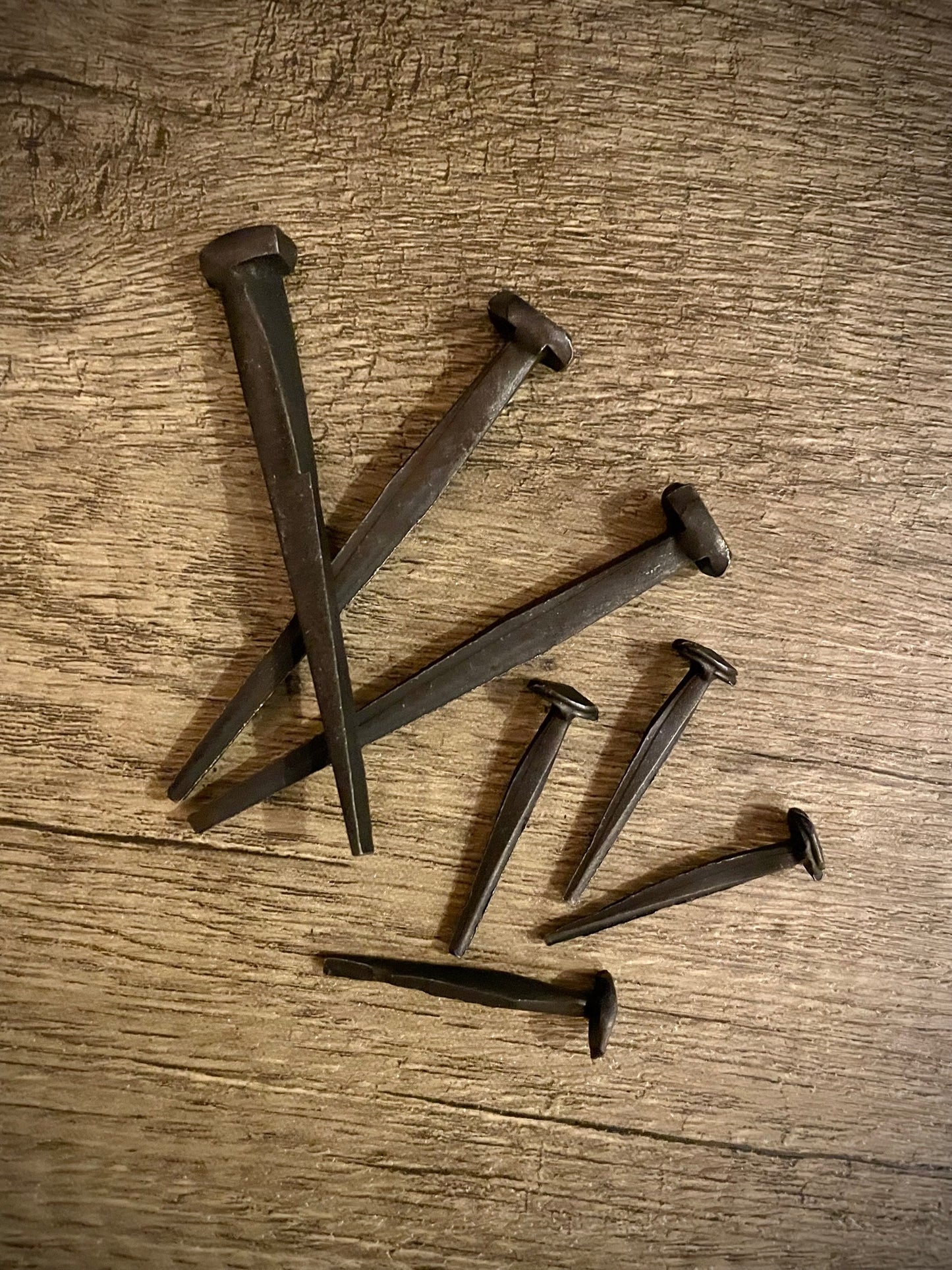 Two sizes of hand-forged iron nails on a rough wood background.