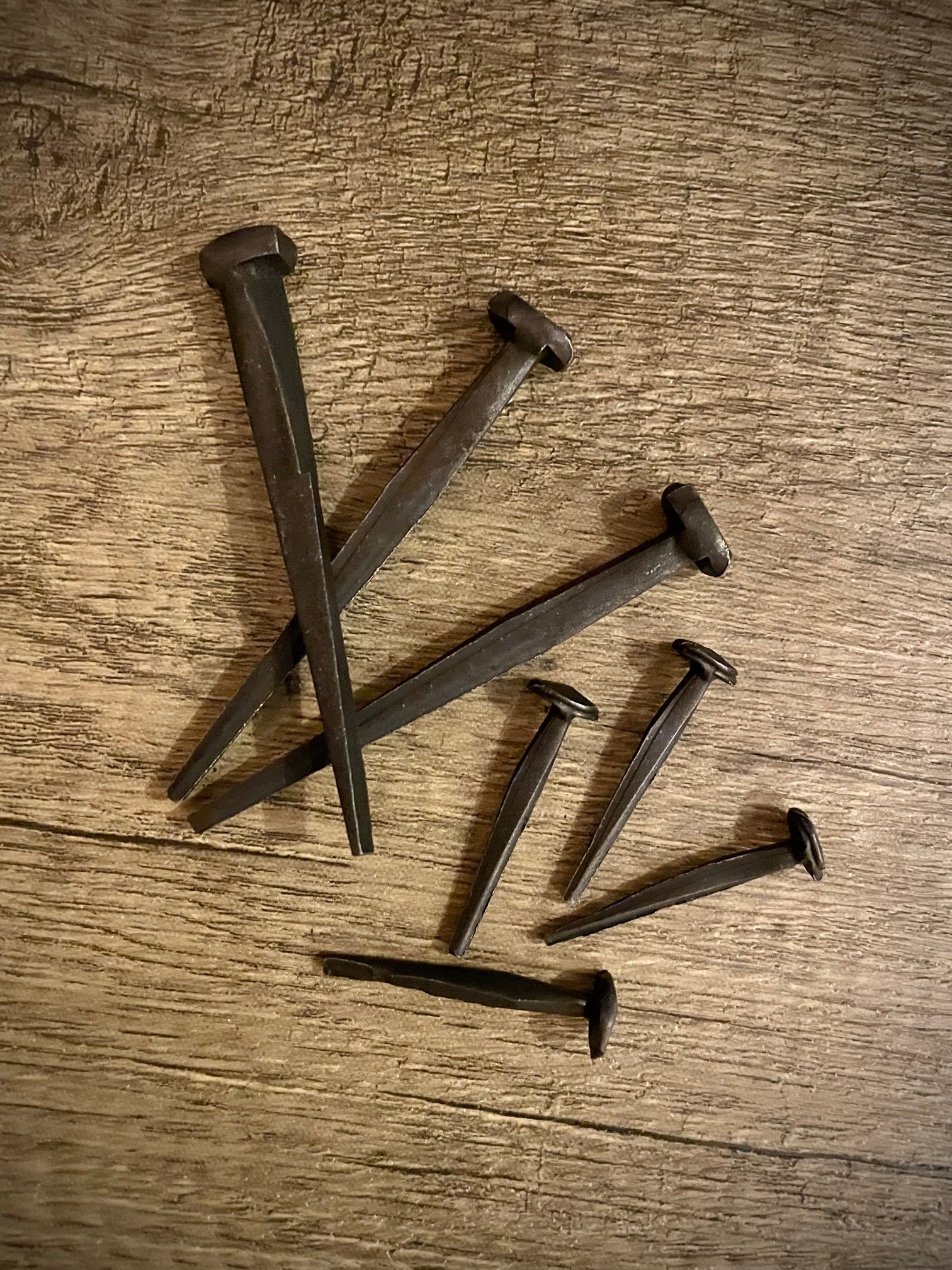Two sizes of hand-forged iron nails on a rough wood background.