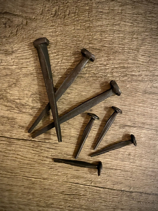 Two sizes of hand-forged iron nails on a rough wood background. 