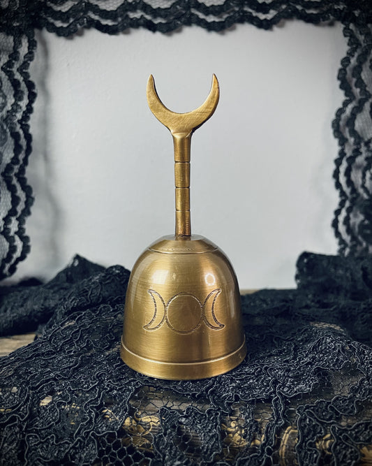 A brass hand bell marked with a triple moon glyph. Its handle ends in a crescent moon. 