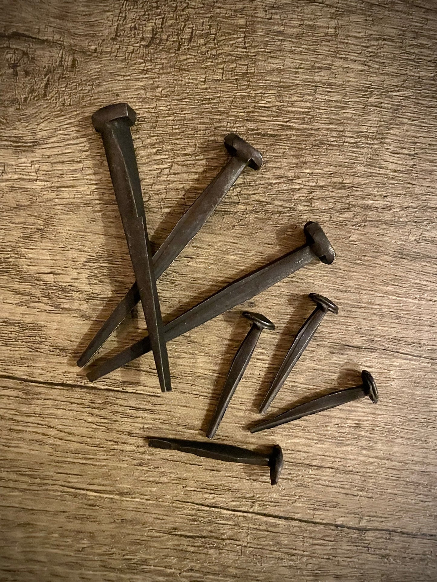 Two sizes of hand-forged iron nails on a rough wood background. 